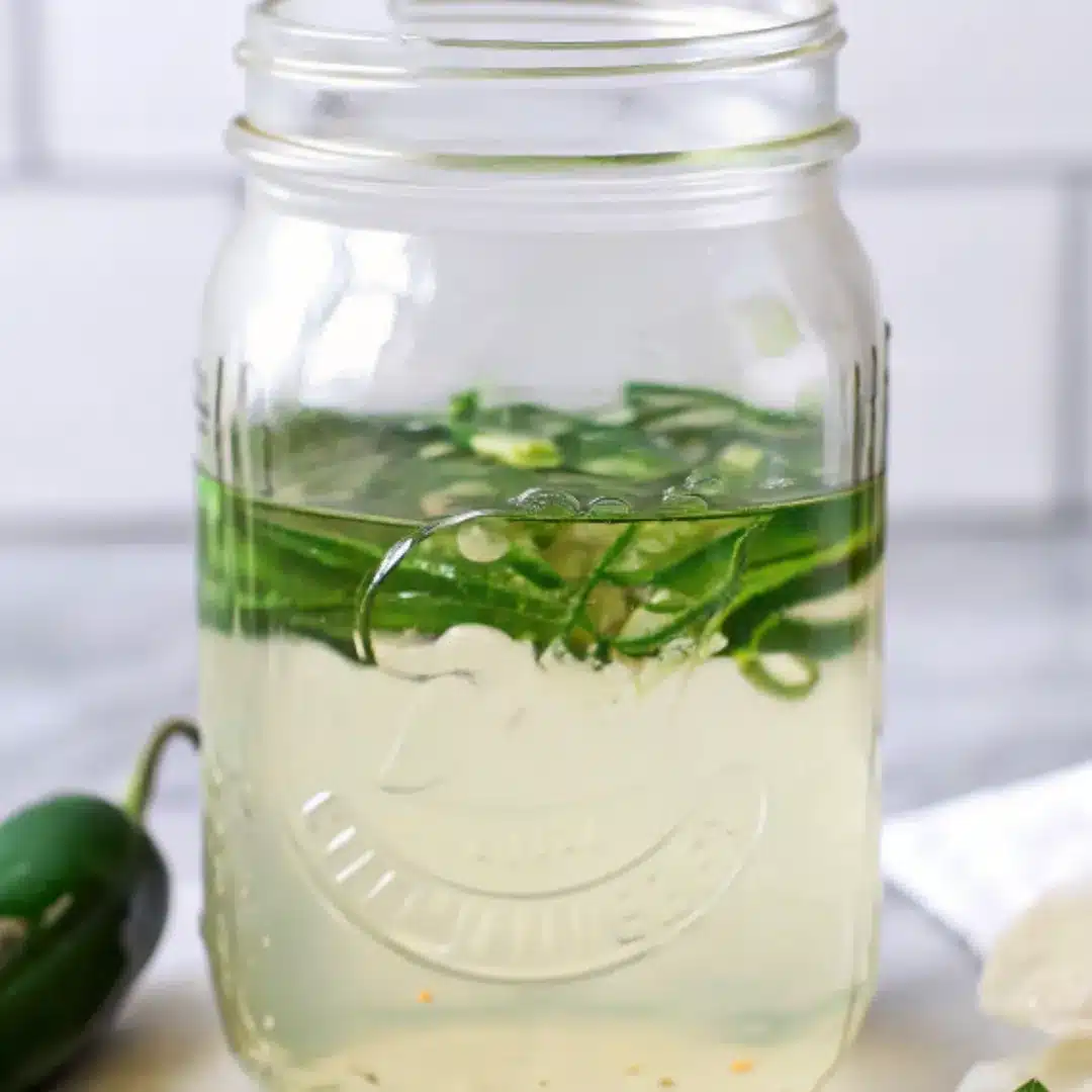Jalapeño Simple Syrup – Sweet Heat in Every Drop Mason jar filled with jalapeño simple syrup and sliced jalapeños in a clear liquid