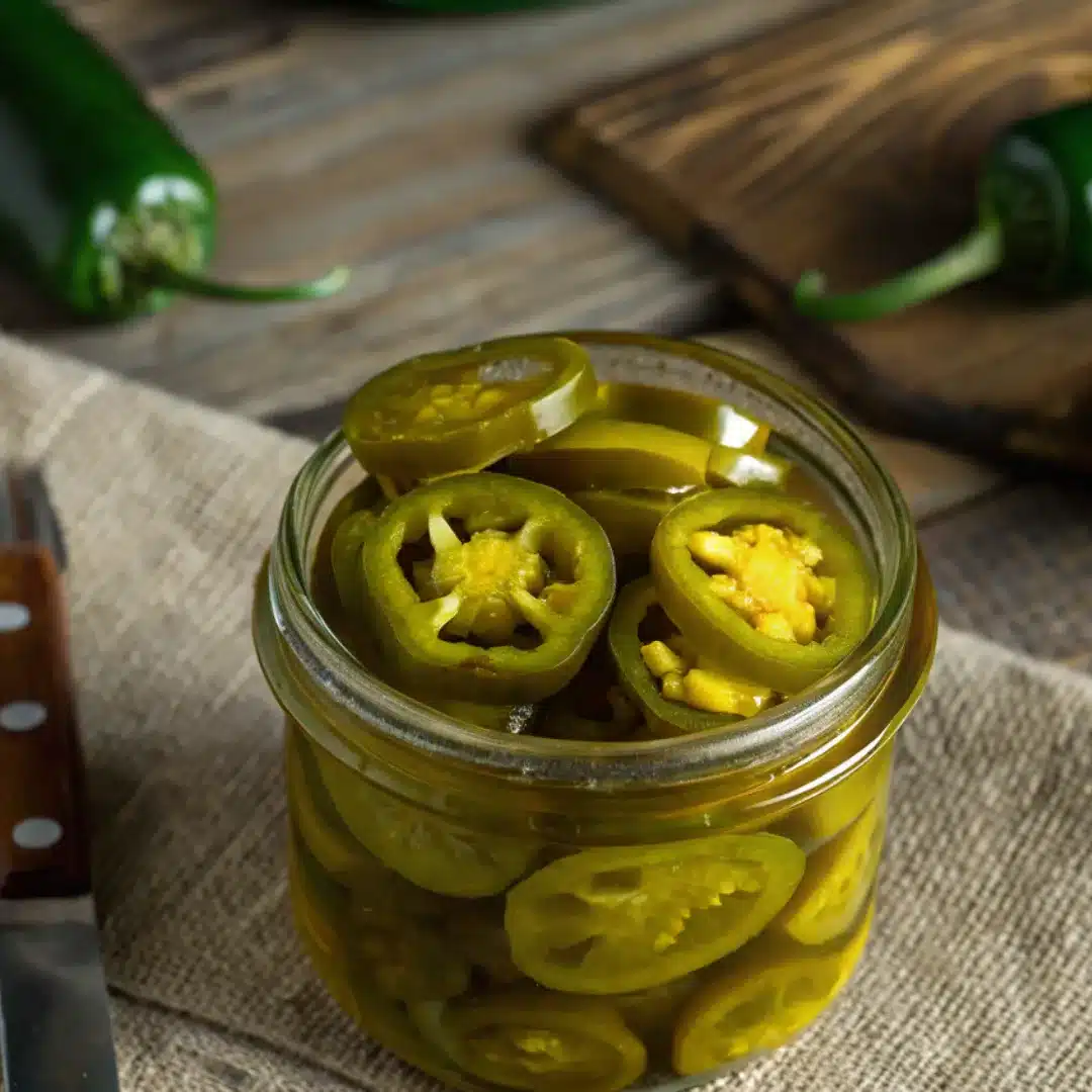 Preserving Jalapeños – Easy Homemade Pickled Peppers Glass jar filled with preserved jalapeño slices on a rustic wooden surface