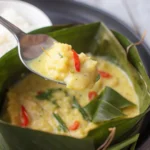 Spoon lifting yellow coconut curry from banana leaf wrap
